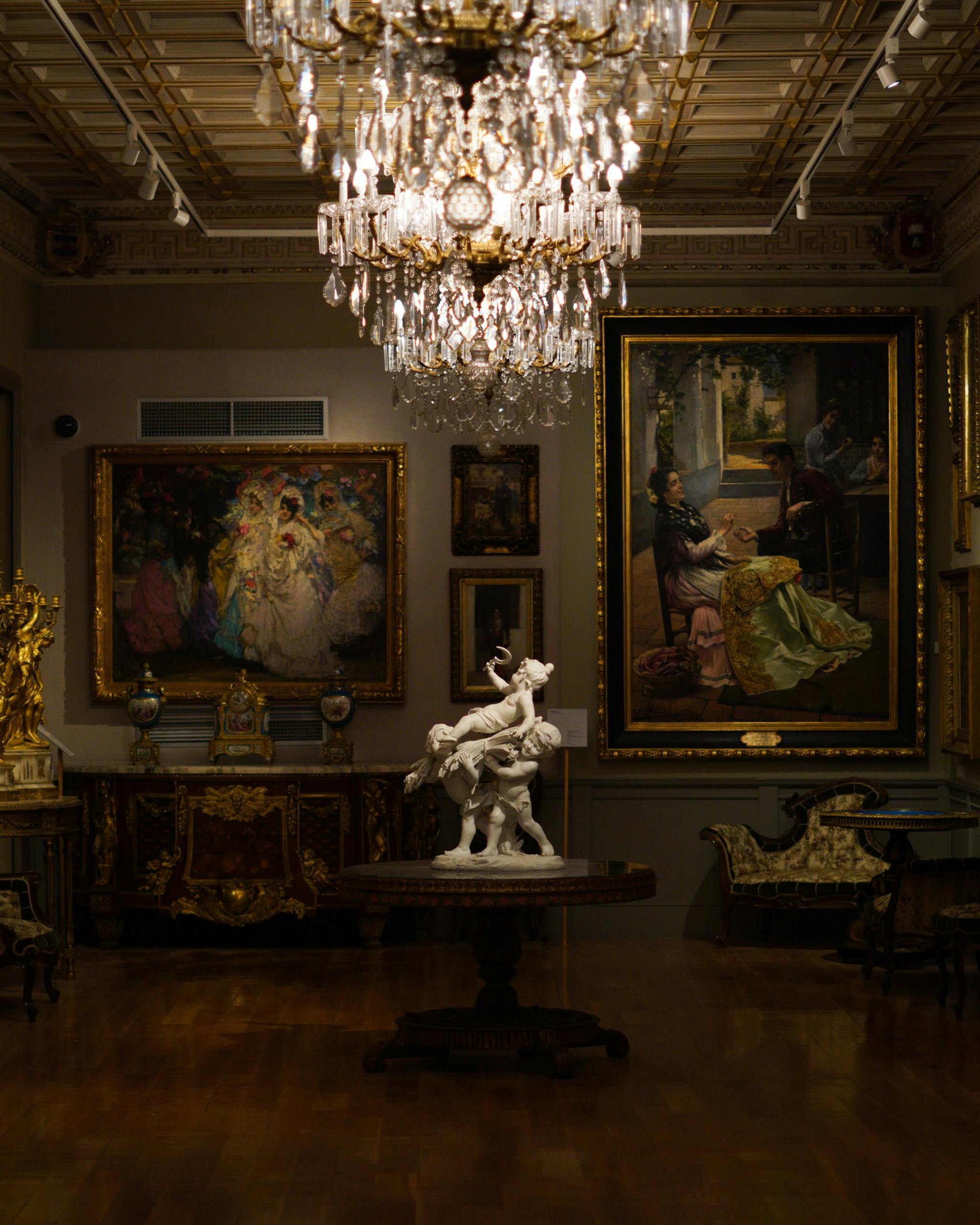 Luxurious art gallery with chandelier, paintings, and sculptures on display.