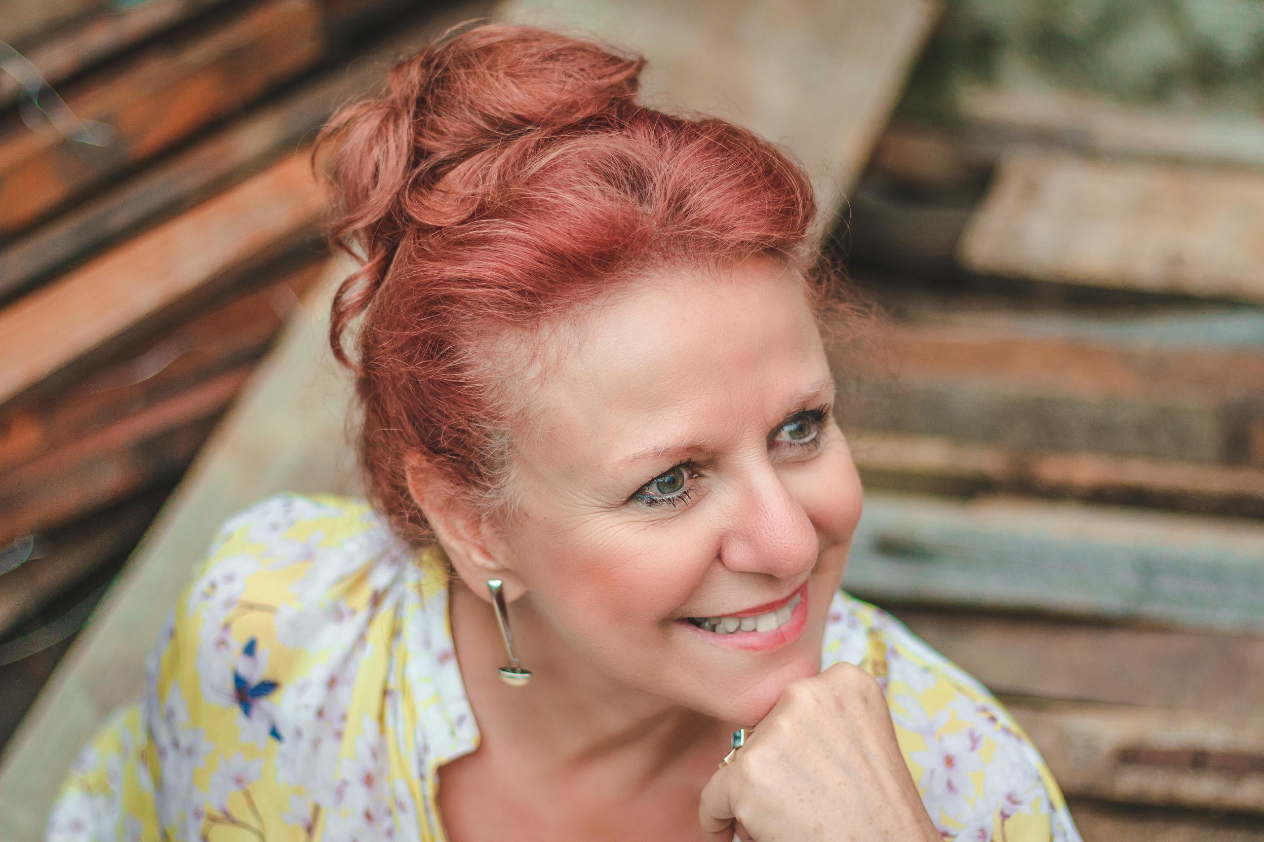 Portrait of a cheerful woman with red hair, wearing a floral blouse, smiling outdoors.