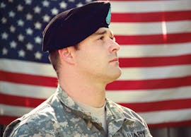 US soldier in uniform stands proudly with the American flag in the background, capturing a sense of patriotism.