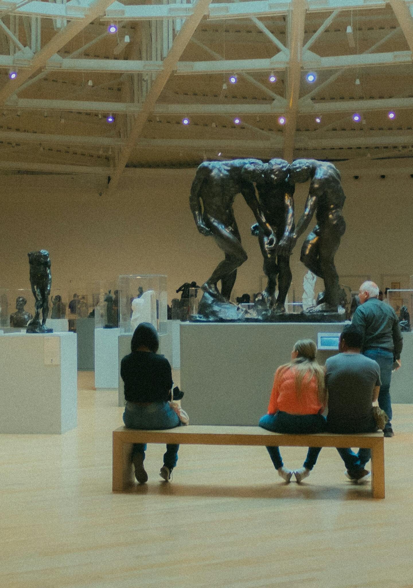Visitors enjoy modern sculptures in a spacious art museum with high ceilings.